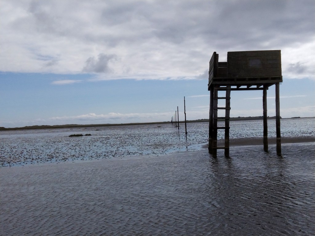 View across the sands with a line of sticks that mark the way and a refuge tower